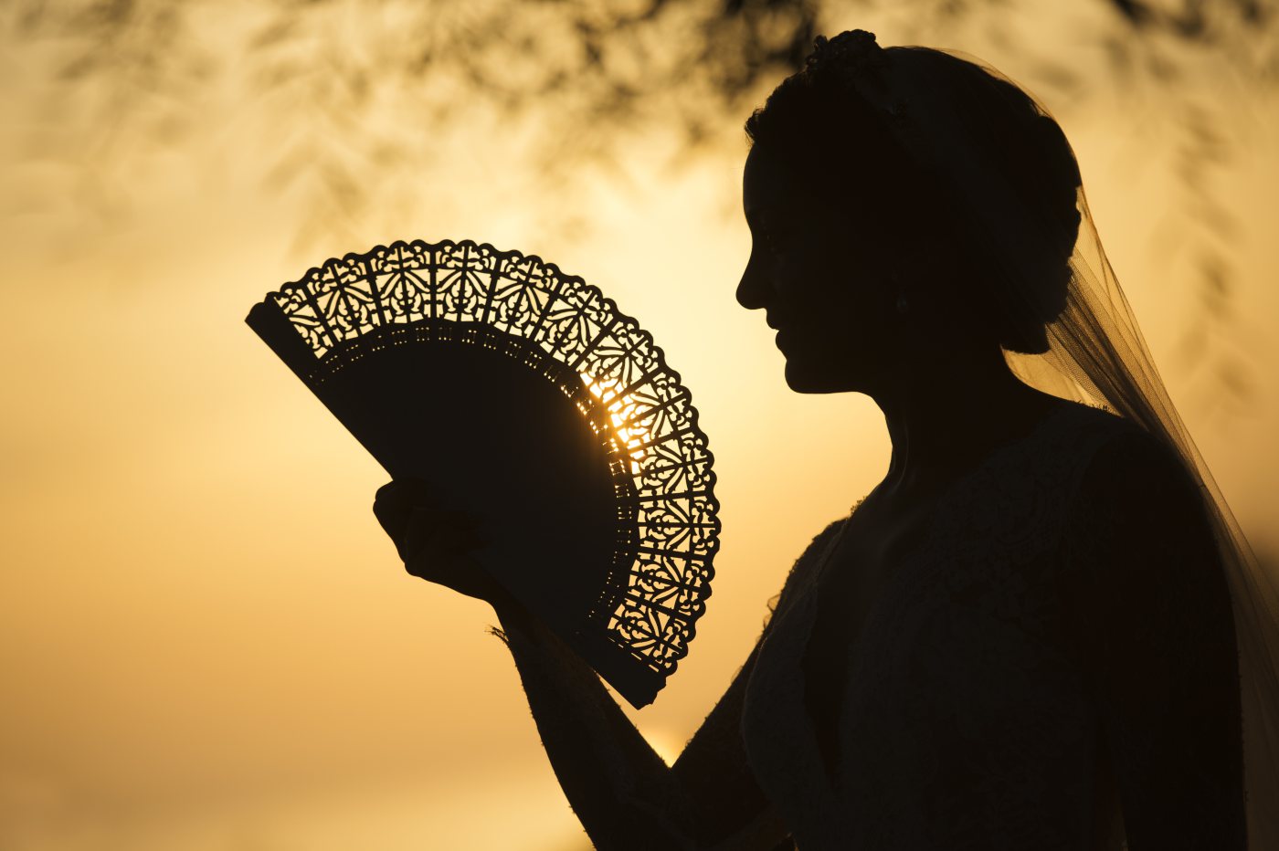 Novia con un abanico calado a contraluz, al atardecer